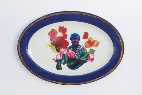 Porcelain. A dark-skinned woman looks off to our right and smiles at the centre of this white oval plate. She is surrounded by flowers and leaves. The cobalt-blue rim is edged in gold.